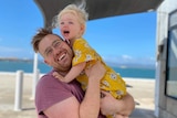 Man smiling at camera with his arms around a little girl