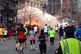 Runners continue to run towards the finish line of the Boston Marathon as an explosion erupts.