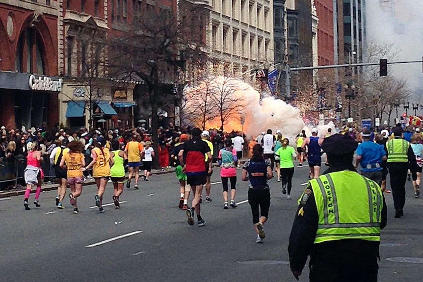 Runners continue to run towards the finish line of the Boston Marathon as an explosion erupts.