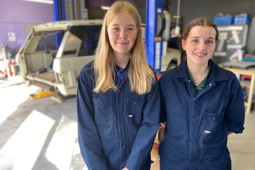 Two teenagers smiling and wearing a blue mechanic outfit. 