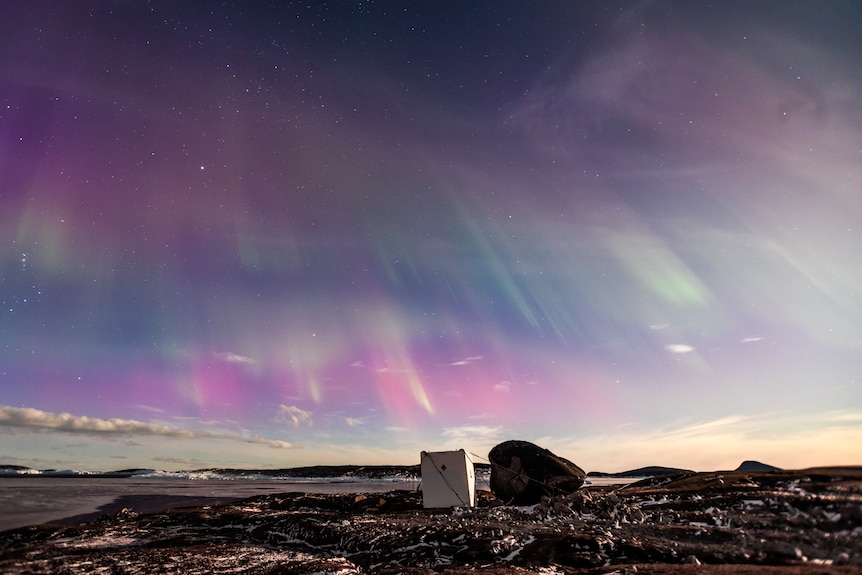 Purple and green auroral lights in bands across the sky with the explosives container at Mawson Station