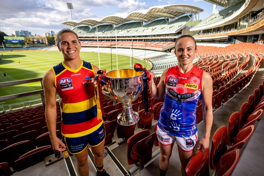 Adelaide's Chelsea Randall and Melbourne's Daisy Pearce smile while holding the cup between them in the Adelaide Oval stands