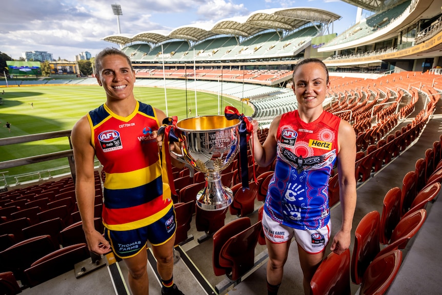 Adelaide's Chelsea Randall and Melbourne's Daisy Pearce smile while holding the cup between them in the Adelaide Oval stands