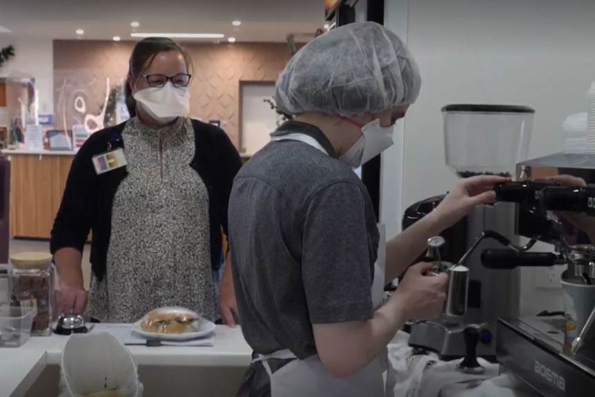 Someone making coffee, with an employee waiting in the background