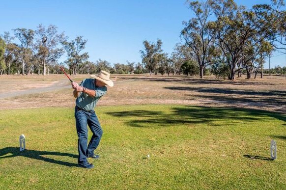 A man in a cowboy hat takes a swing on a golf course