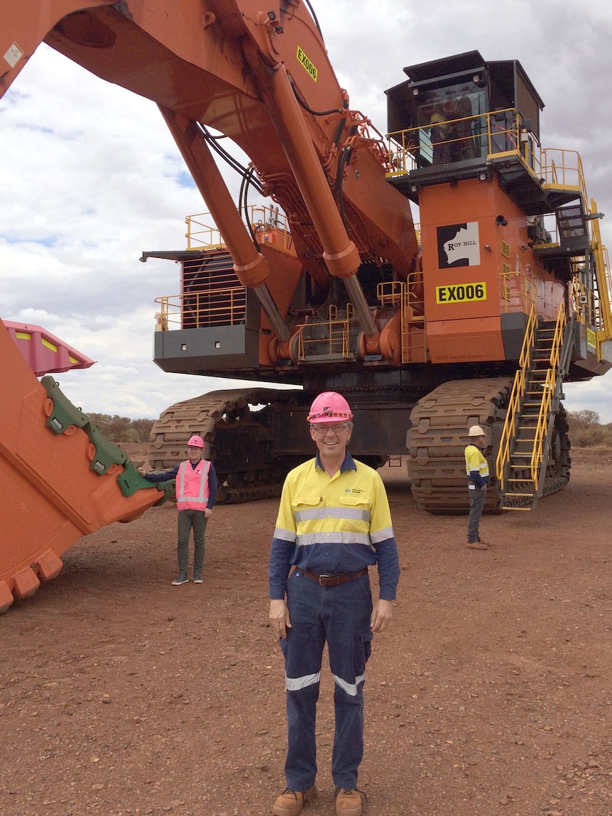 Man in work gear and pink hard hat standing in front of large mining digger