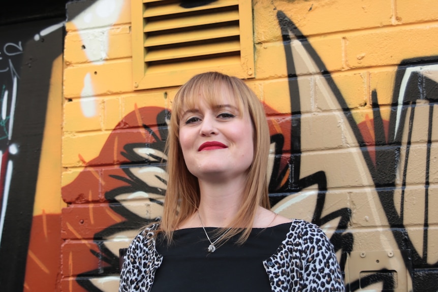 A woman with blonde hair in front of a coloured wall