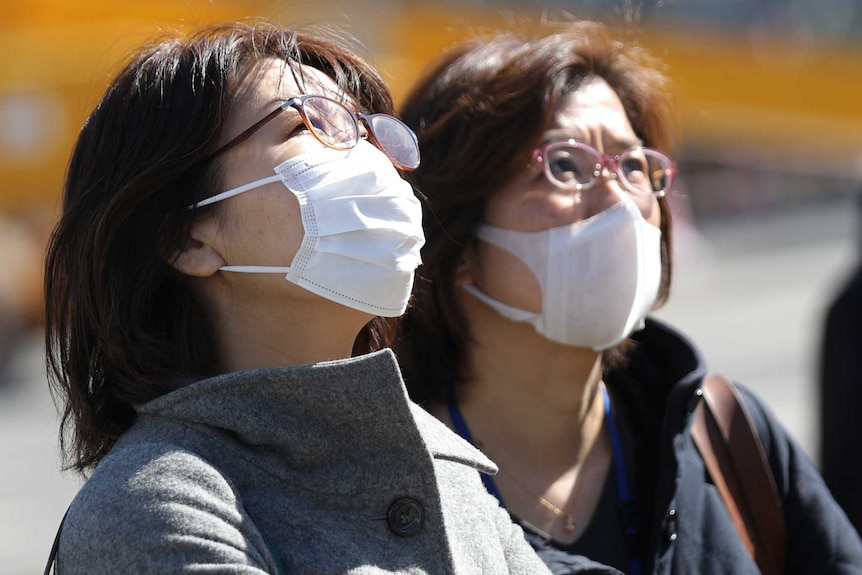 Two women in heavy coats wear face masks while walking outside.