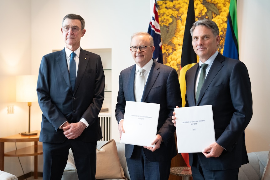 Three men in suits — Angus Houston, Anthony Albanese and Richard Marles — pose for a photo holding white documents