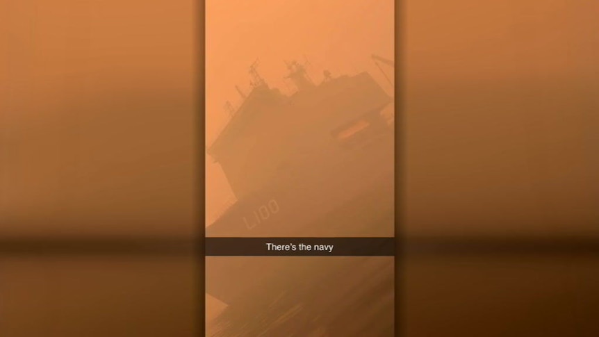 A still from a Snapchat video showing a navy ship anchored in water, surrounded by red-orange smoke.