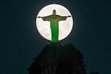 The moon descends behind the statue of Christ the Redeemer in Rio, lit by the colours of Brazil.