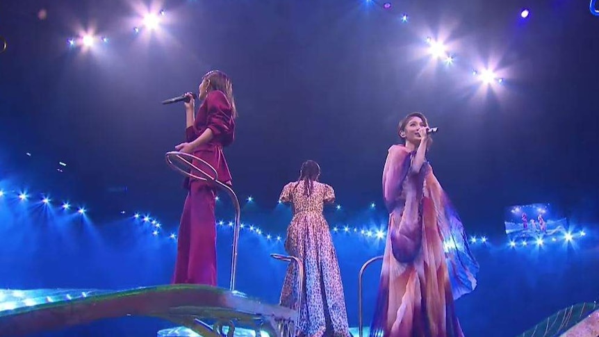 Three women perform on stage with lights