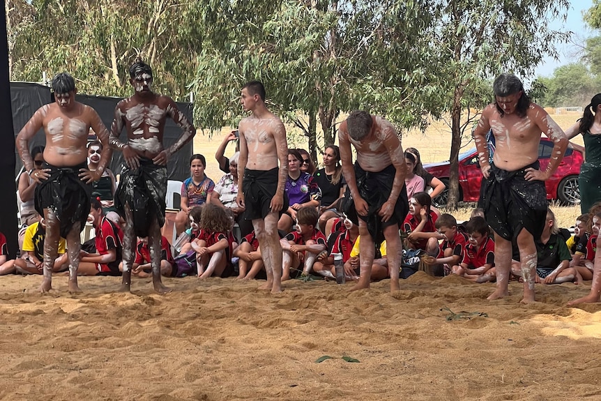Aboriginal men in black loin cloths and painted up dance on the sand