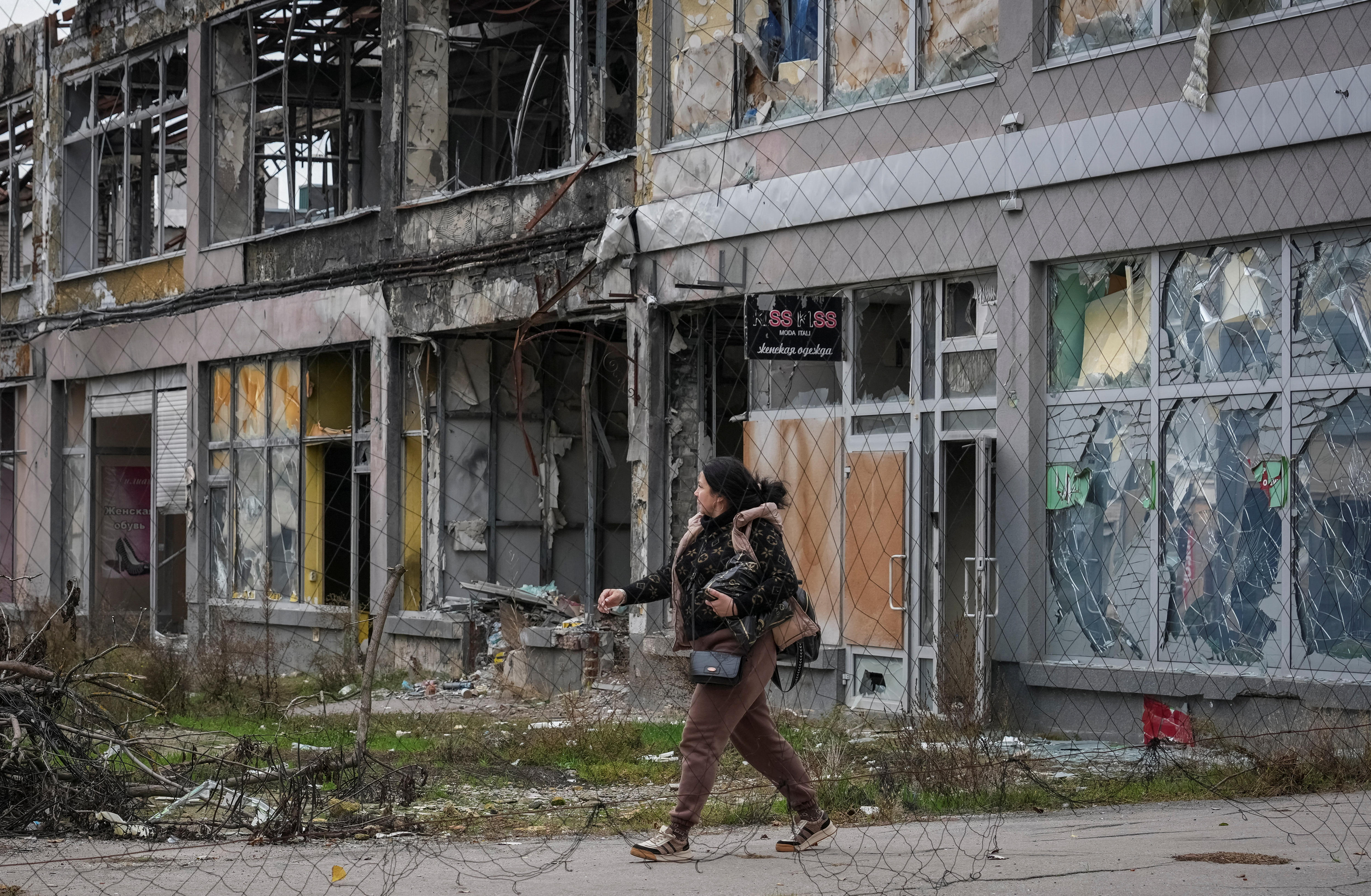 A woman walking out of a damaged building with anti-drone netting in the foreground.