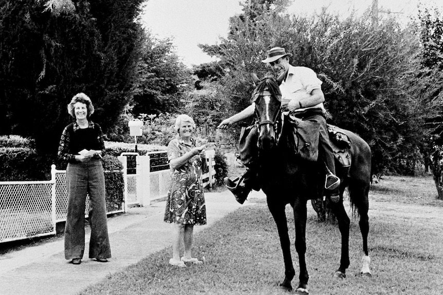 A man on a horse hands an envelope to a woman. They are smiling