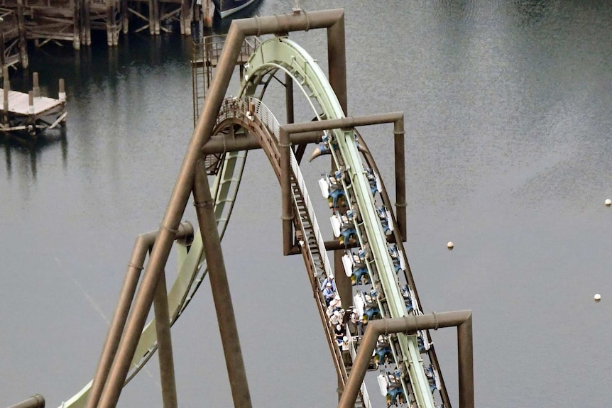 the tracks of a roller coaster curve sharply in the air, with riders stuck in their seats, upside down just past the top