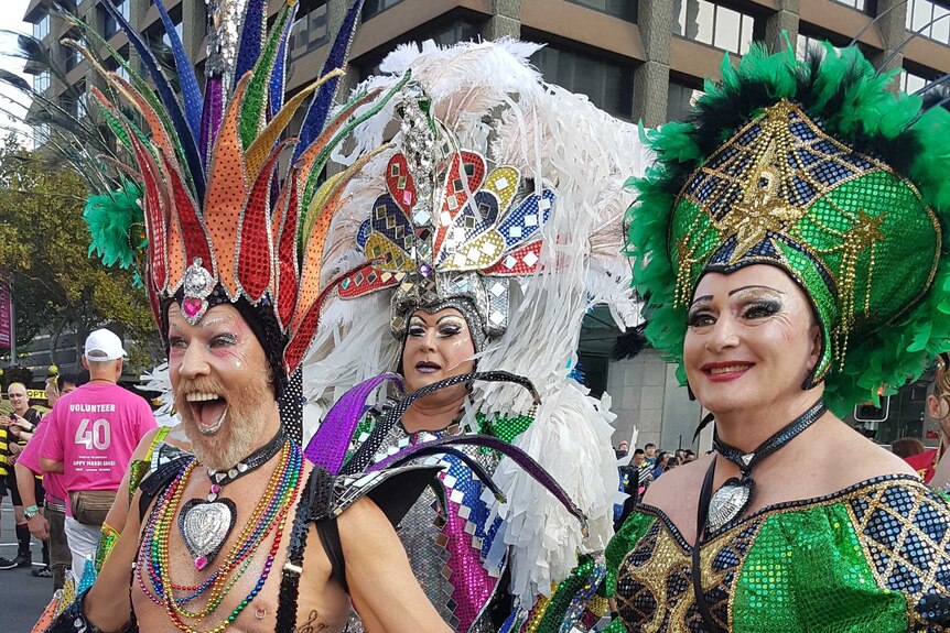 Three people dressed in bright sequined costumes pose on a Sydney street.
