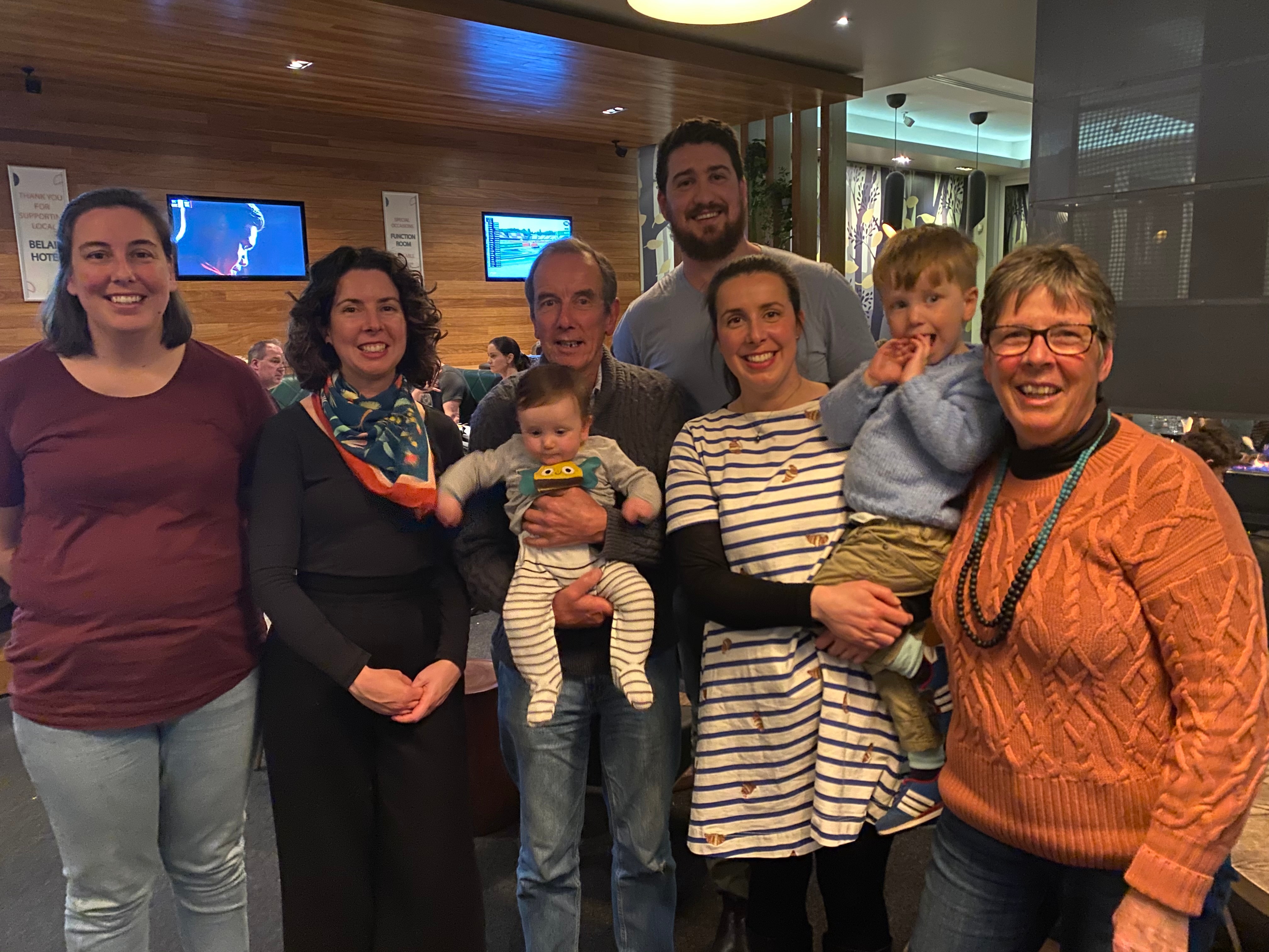 Group of men women, a child and a baby standing together for a family photo.