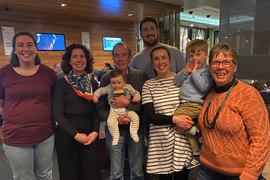 Group of men women, a child and a baby standing together for a family photo.