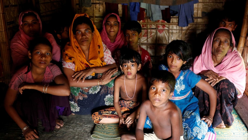 A group of people, including women and children, sit huddled together in a dark room