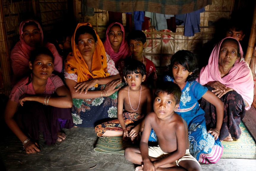 A group of people, including women and children, sit huddled together in a dark room