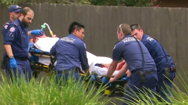 Police and paramedics surround a man on a stretcher being led into an ambulance
