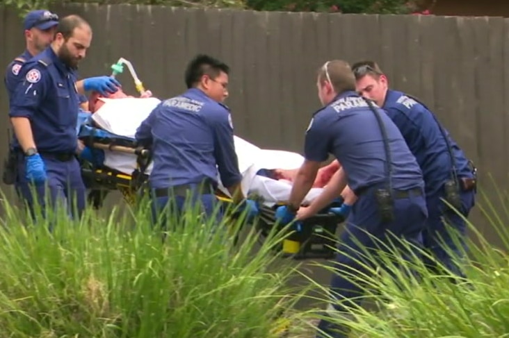 Police and paramedics surround a man on a stretcher being led into an ambulance