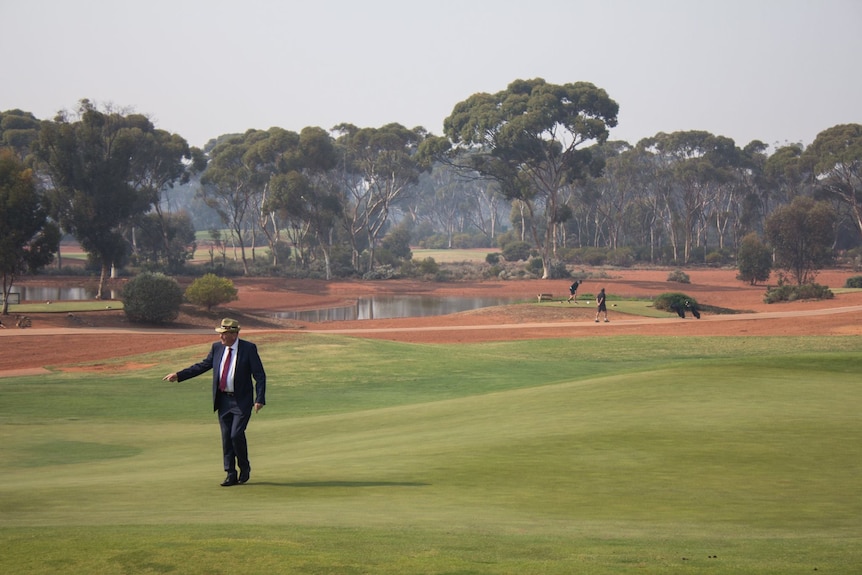 Un homme en costume marchant sur le fairway d'un parcours de golf en herbe.  