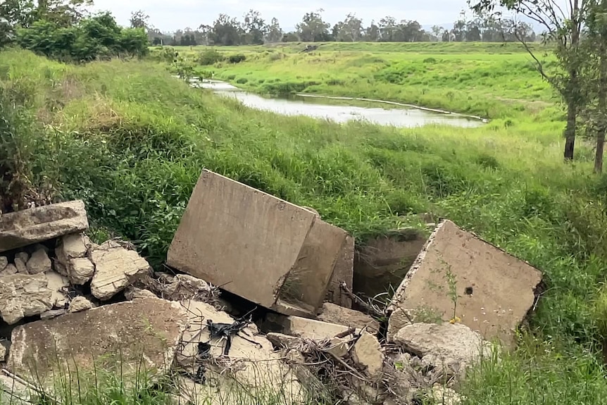 Concrete culverts or pipes damaged by flooding in a field near a waterway.