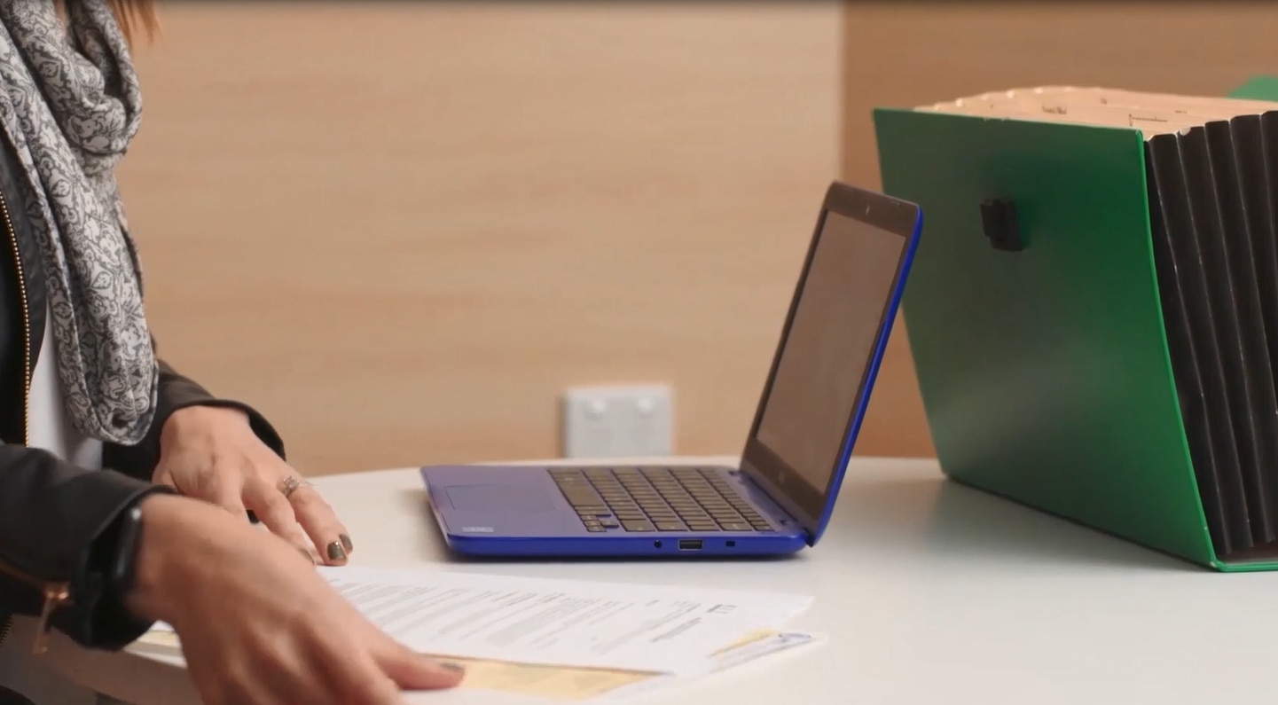 A person sitting at a table with a laptop, a few sheets of paper and a document folder