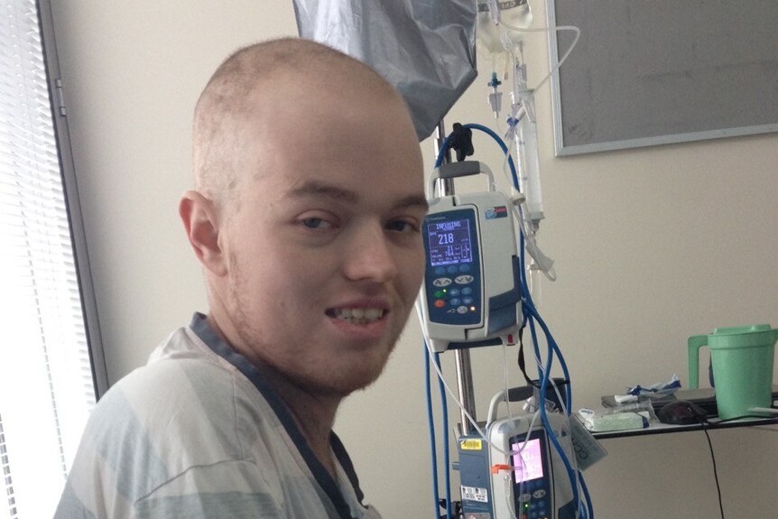A man with a shaved head sitting next to an IV machine.