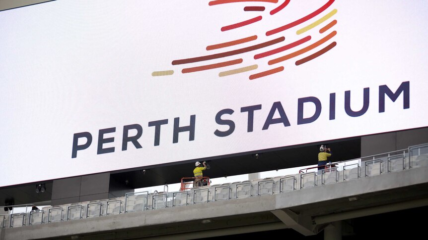 Workmen in high viz and hard hat put up Perth Stadium sign, inside the new stadium.