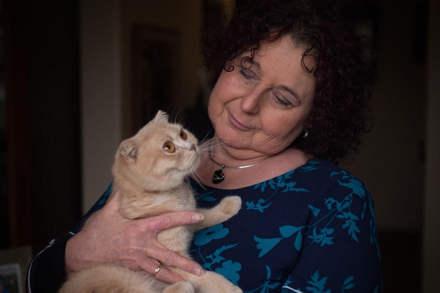 A middle-aged woman looks at the cat she is holding in her arms.