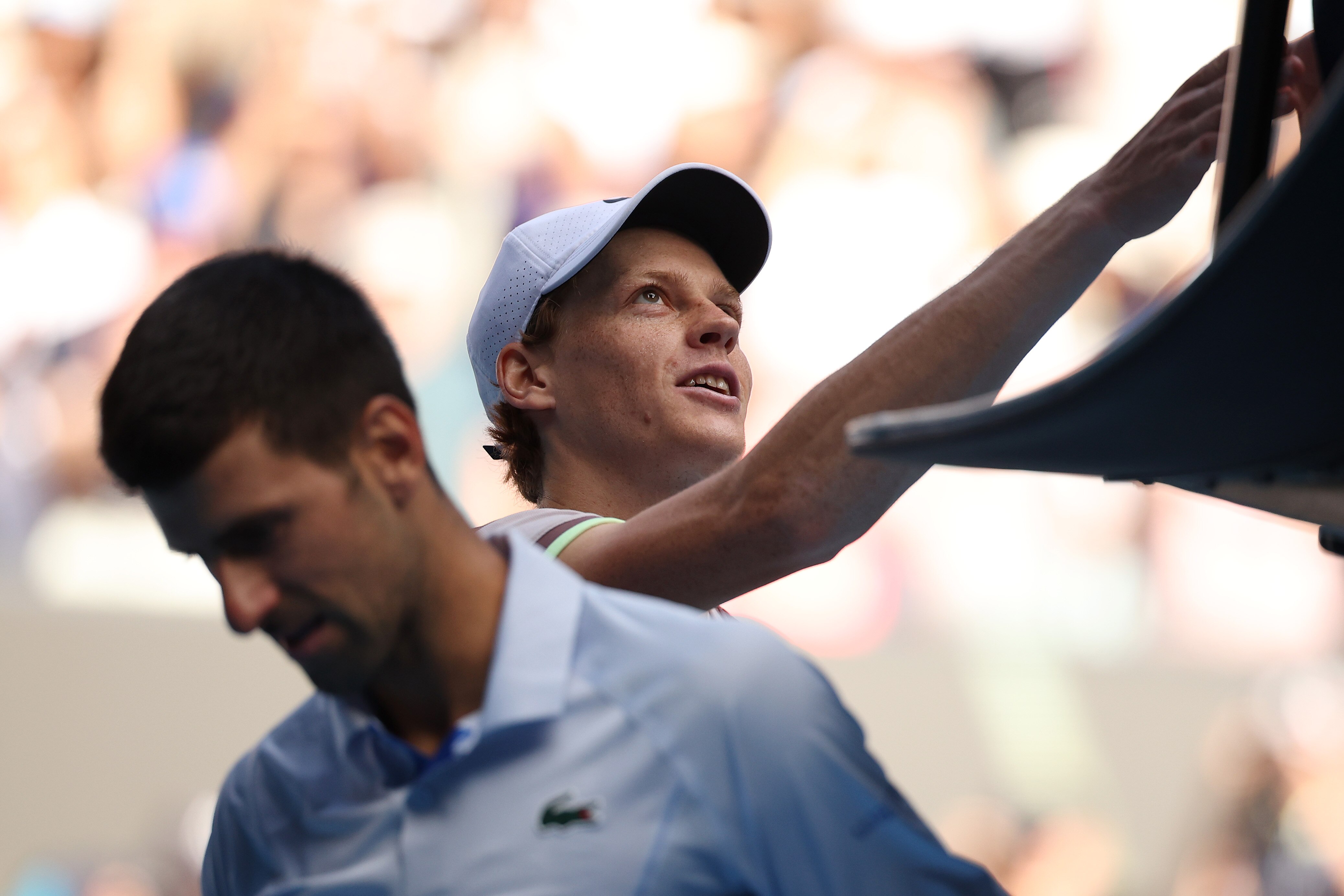 Novak Djokovic is blurry in the foreground as Jannik Sinner shakes the umpire's hand after their match at the Australian Open.