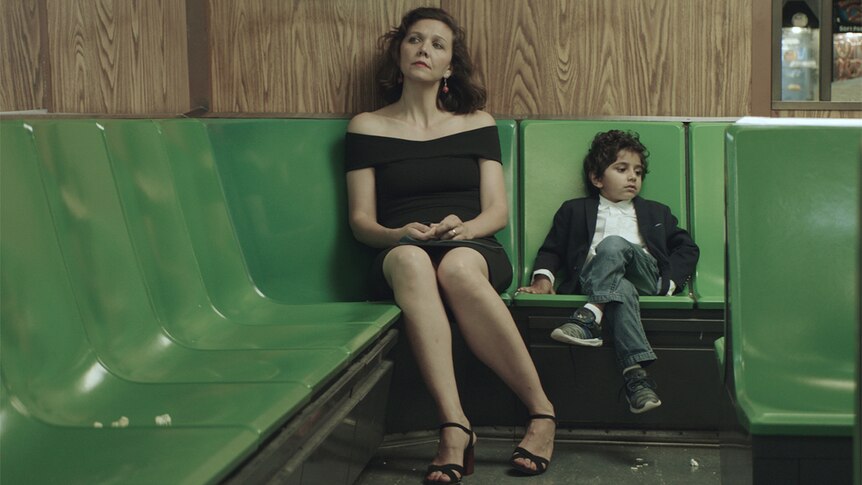 Colour still of Maggie Gyllenhaal and Parker Sevak sitting on bank of green seats in 2018 film The Kindergarten Teacher.