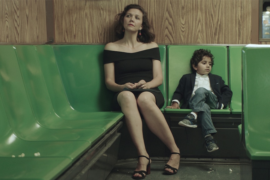Colour still of Maggie Gyllenhaal and Parker Sevak sitting on bank of green seats in 2018 film The Kindergarten Teacher.