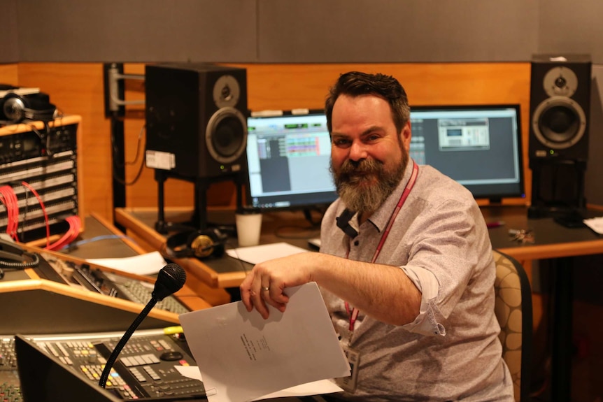 Audio engineer in studio surrounded by audio equipment.