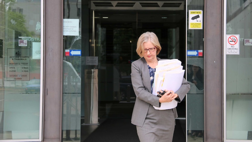 A woman exits a building while holding folders.