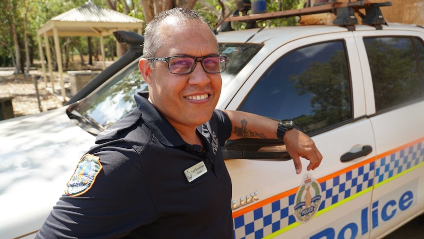 Senior Constable Karl Gunderson stands by a NT Police car and smiles warmly at the camera. He is wearing a police uniform.