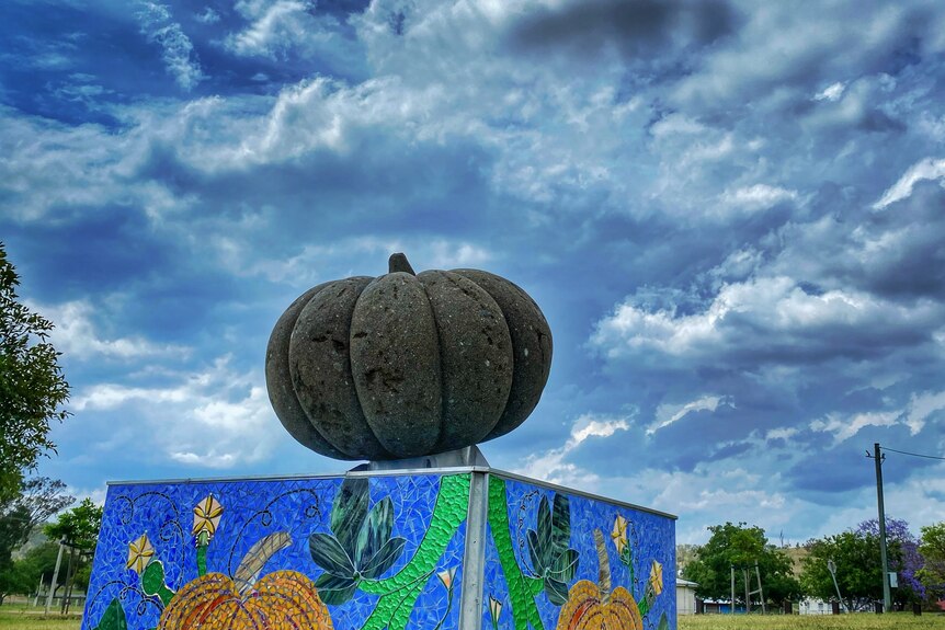 dark green pumpkin statue mounted on box with blue and grey looming clouds in the background