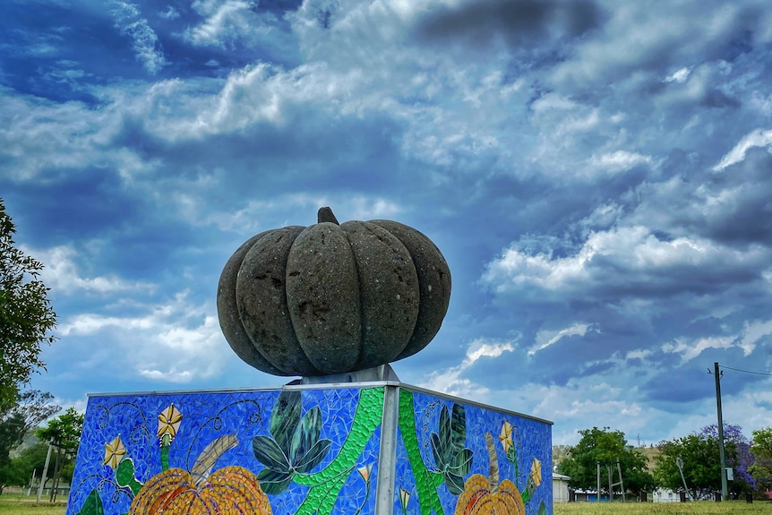 dark green pumpkin statue mounted on box with blue and grey looming clouds in the background