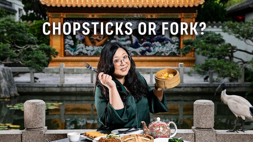  Woman with glasses holding a fork and bamboo steamer; text "CHOPSTICKS OR FORK?" above; Asian garden backdrop with a bird.