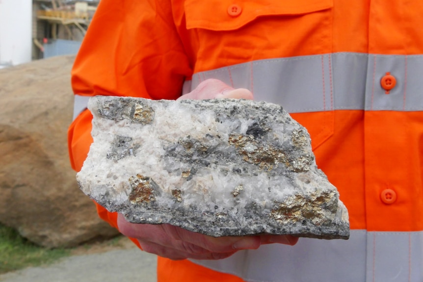 A person in a high-vis shirt holds a chunk of rocks containing small amounts of gold.