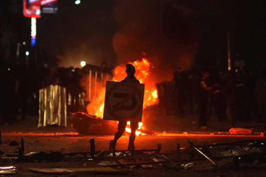 A protester uses a road sign as a shield during clashes with police in Makassar, Indonesia.
