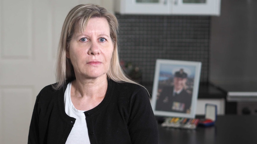 Julie-Ann Finney looking straight ahead with a framed photo of David Finney in the background.