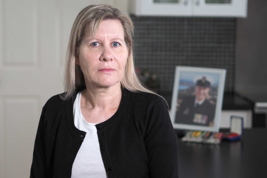 Julie-Ann Finney looking straight ahead with a framed photo of David Finney in the background.