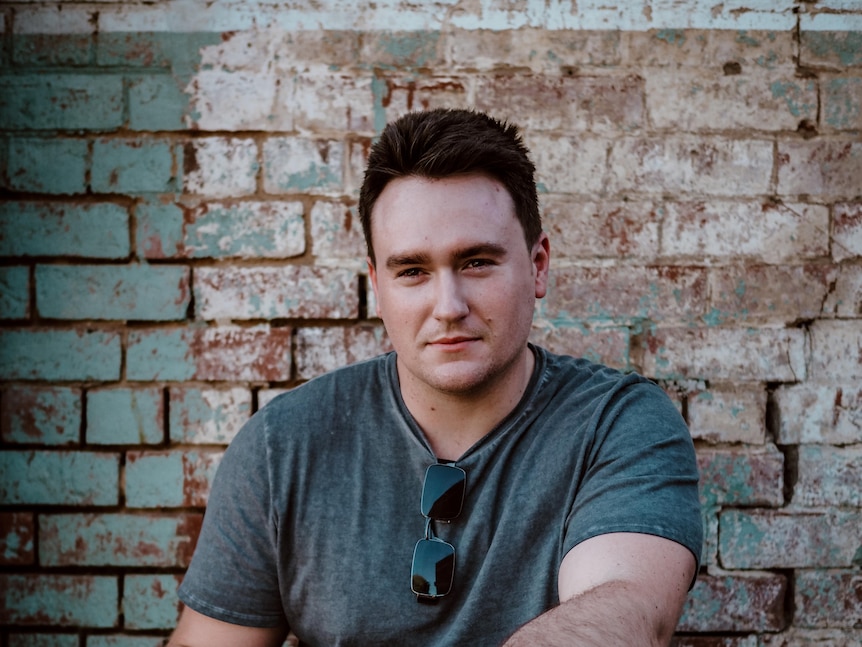 Jason Clymo sitting in front of a white and brown brick wall.