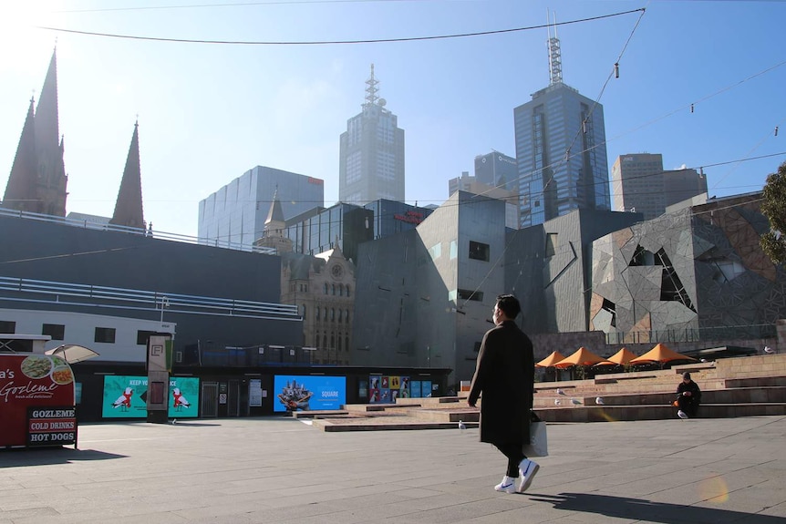 A man in a facemask walks past Melbourne's Federation Square, which is empty