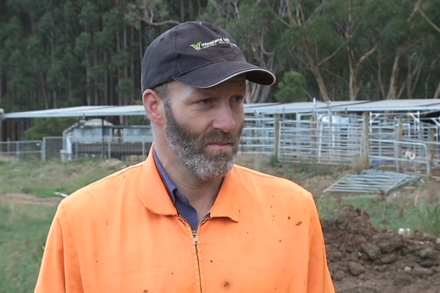 craig wears a hat and overalls, standing in front of his dairy in the early morning light