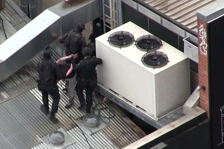 Police surround a handcuffed man on the roof of a building